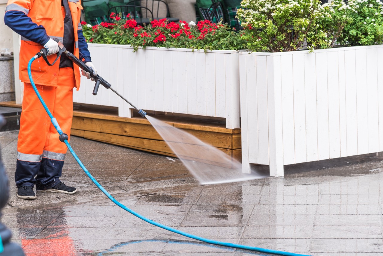 Worker washes the sidewalk in front of a street cafe - surface sanitation