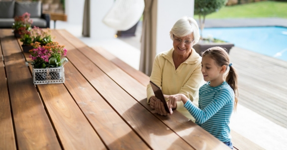 Granddaughter and grandmother discussing over a digital tablet in deck shade