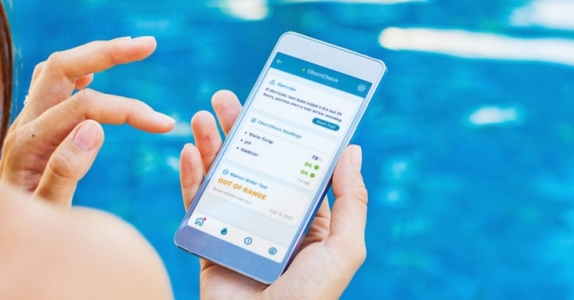 woman sitting poolside on her phone showing water chemistry on phone, pool automation