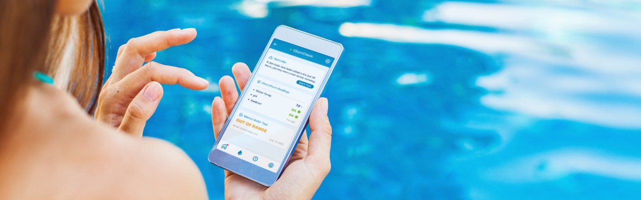 woman sitting poolside on her phone showing water chemistry on phone, pool automation