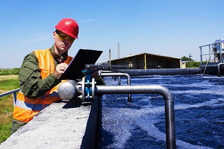 A man in a red helmet and safety vest examining pipes for water treatment.