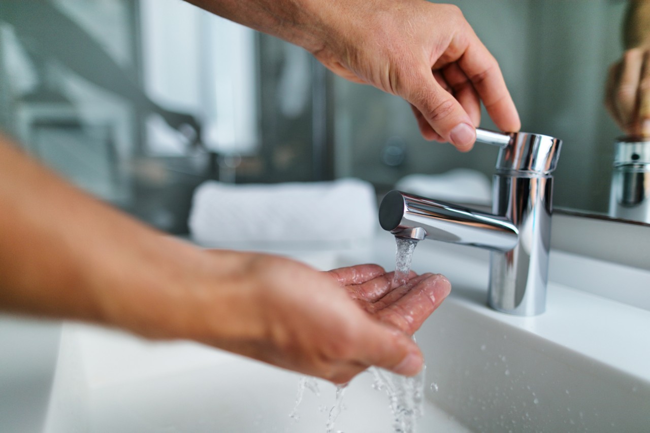 Man washing hands in bathroom sink at home checking temperature touching running water with hand. Closeup on fingers under hot water out of a faucet of a sink; Adobe Stock, 188032490