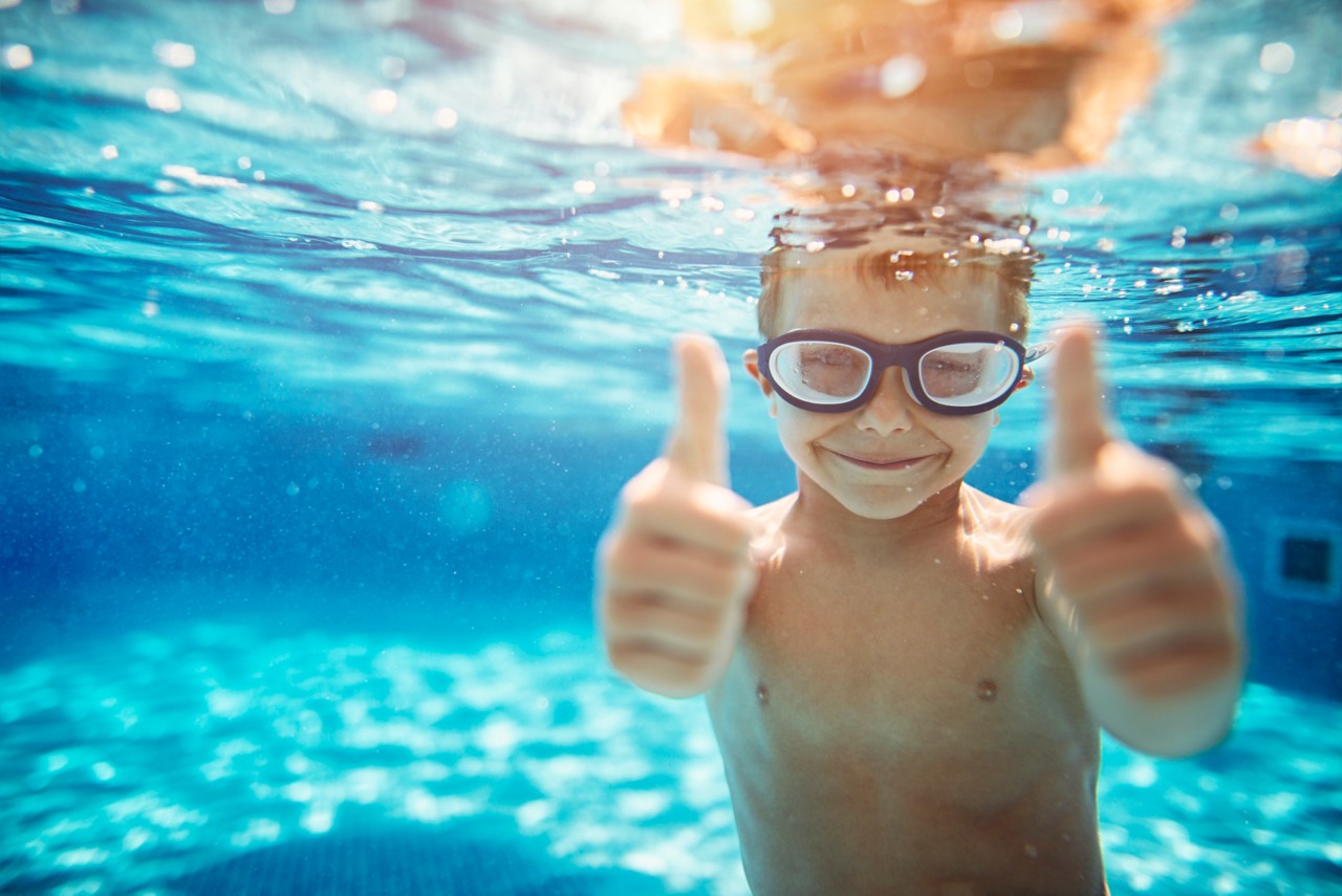 young-boy-in-goggles-swimming-underwater-in-blue-pool-thumbs-up-horizontal-7360x4912-image-file-670950038